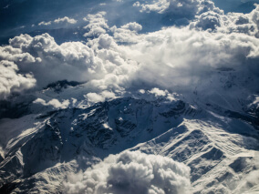 Фото. Заснеженные горные вершины в облаках, вид сверху.